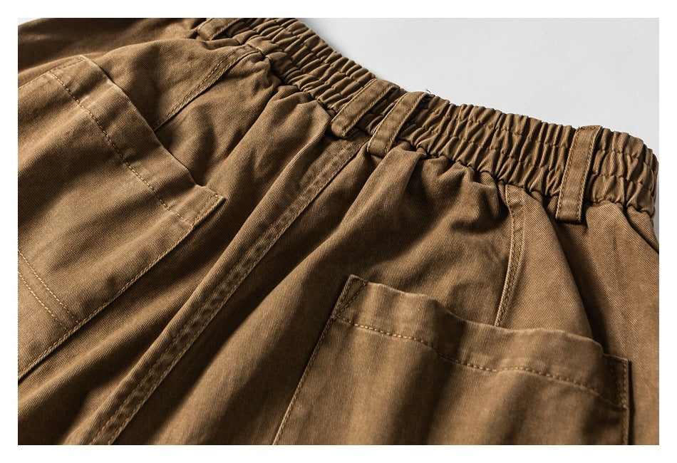 Close-up of brown trousers showing the elasticated waistband, belt loops, front fly and pocket edges.