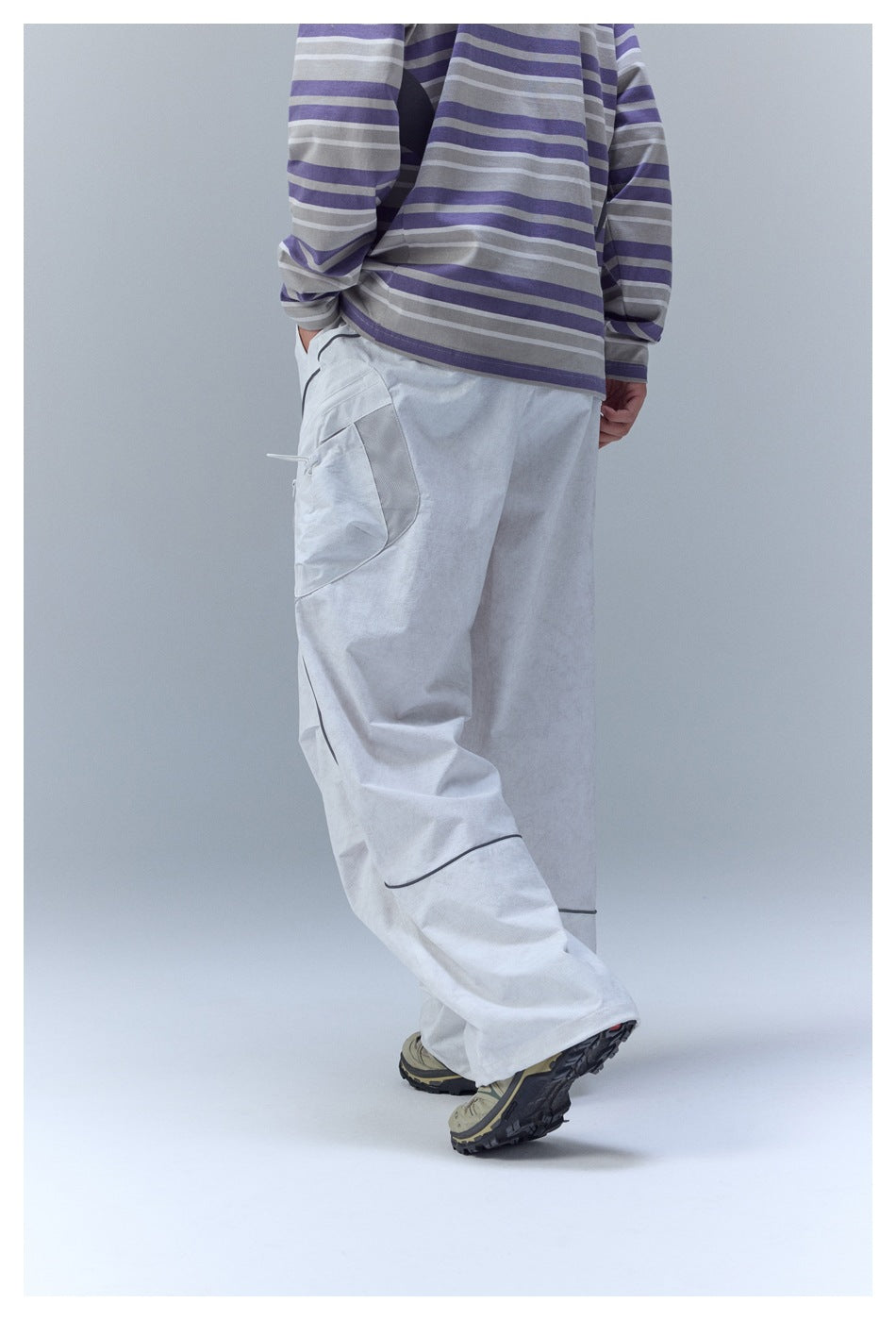 Rear view of a model wearing loose light gray cargo pants and a gray-and-purple striped shirt.