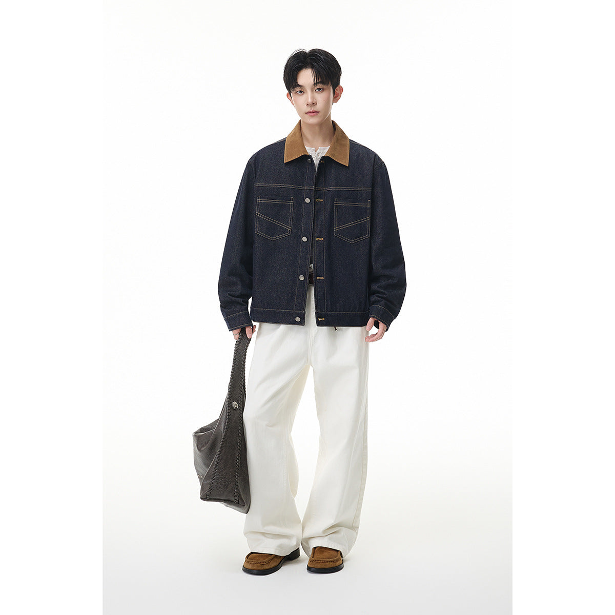 Full-length model wearing a dark indigo jacket with a tan collar and white wide-leg trousers, carrying a dark bag.