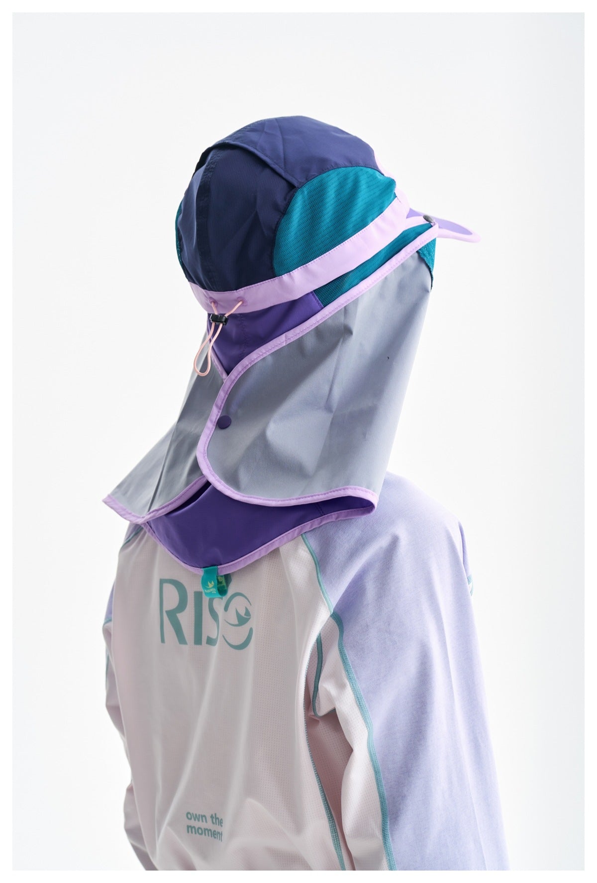 Close-up of a navy, teal, and lavender sun cap with a long neck flap, worn over a white and lavender top.