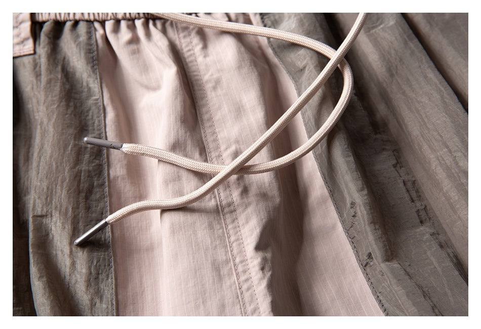 Close-up of pale drawstrings with metal tips against the beige and crinkled gray panels of the shorts.