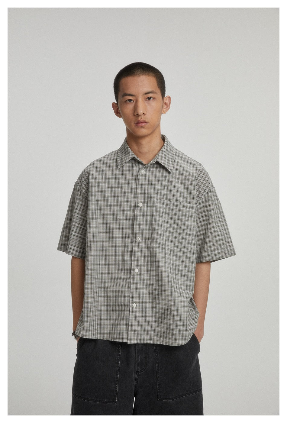 Model wearing a gray check short-sleeve button-up shirt with chest pocket and black wide-leg denim shorts