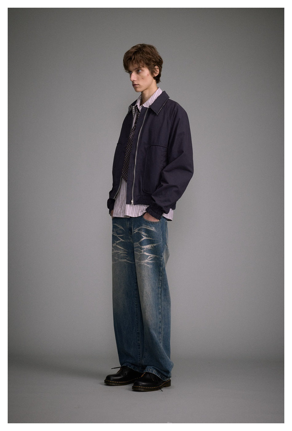 Model in a dark navy zip-front jacket with a pointed collar, large pockets and elastic cuffs, shown at a three-quarter angle.