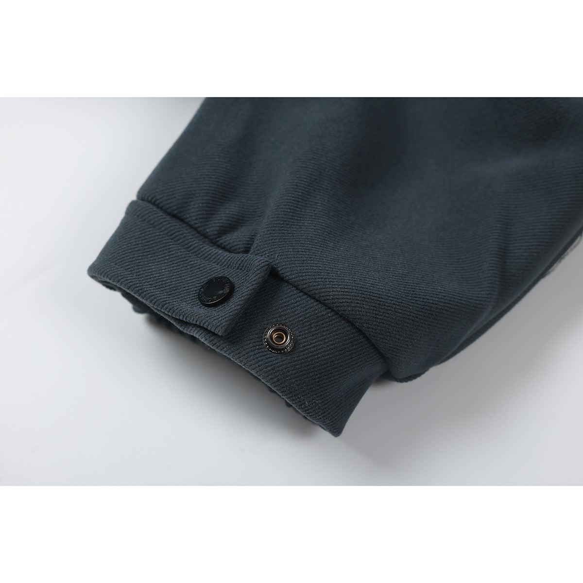 Close-up of a dark charcoal jacket cuff with a snap tab and black button.