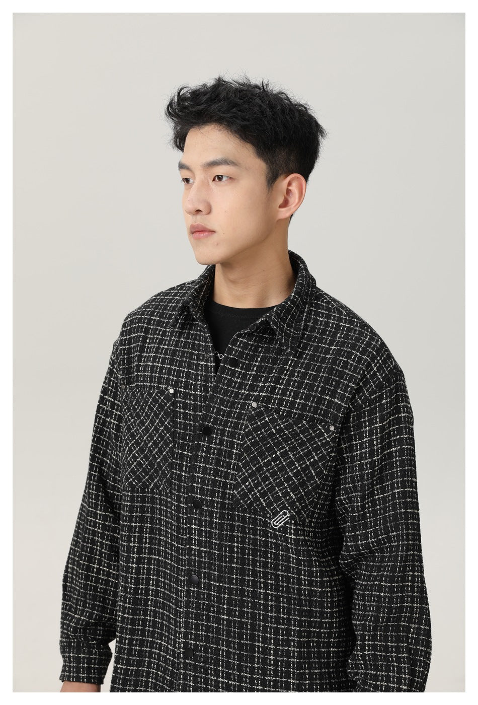 Close view of a model wearing a black-and-white grid overshirt, showing its collar, snap buttons, and chest pockets.