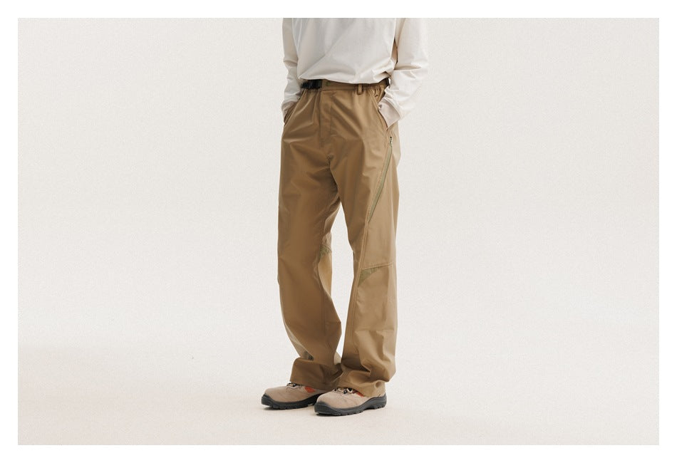 Front three-quarter view of a person wearing tan pants with diagonal zip pockets and hiking shoes.