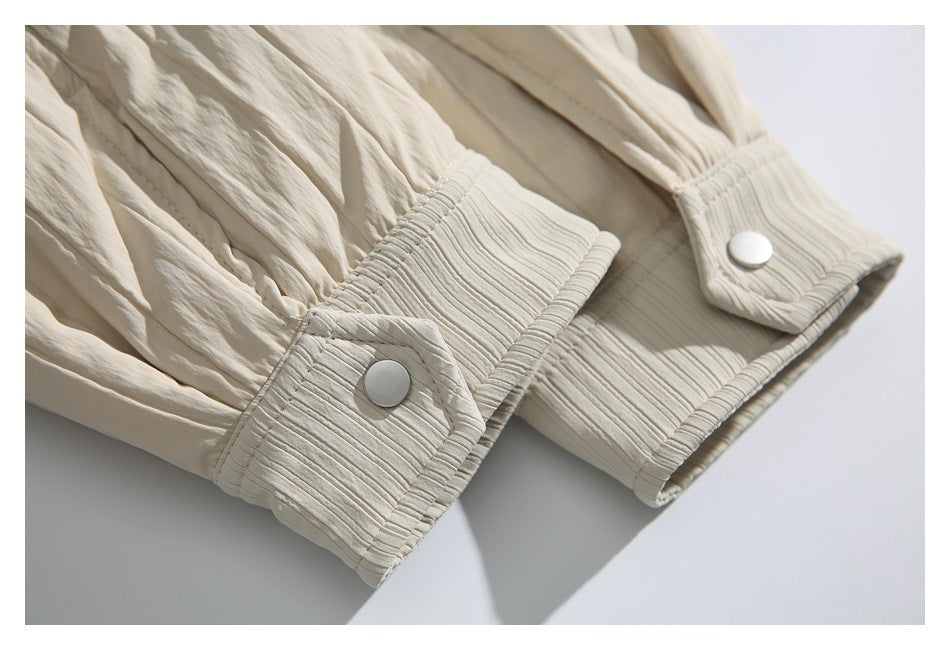 Close-up of cream garment cuffs with gathered sleeves, ribbed trim and round white snap buttons.