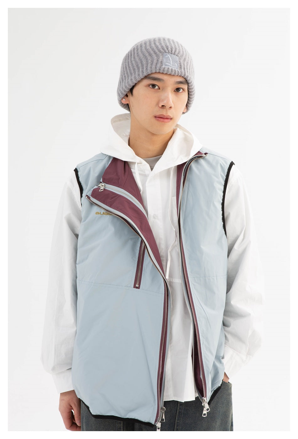 Close view of a pale blue vest with burgundy zip panels and a gray ribbed beanie worn by a model.