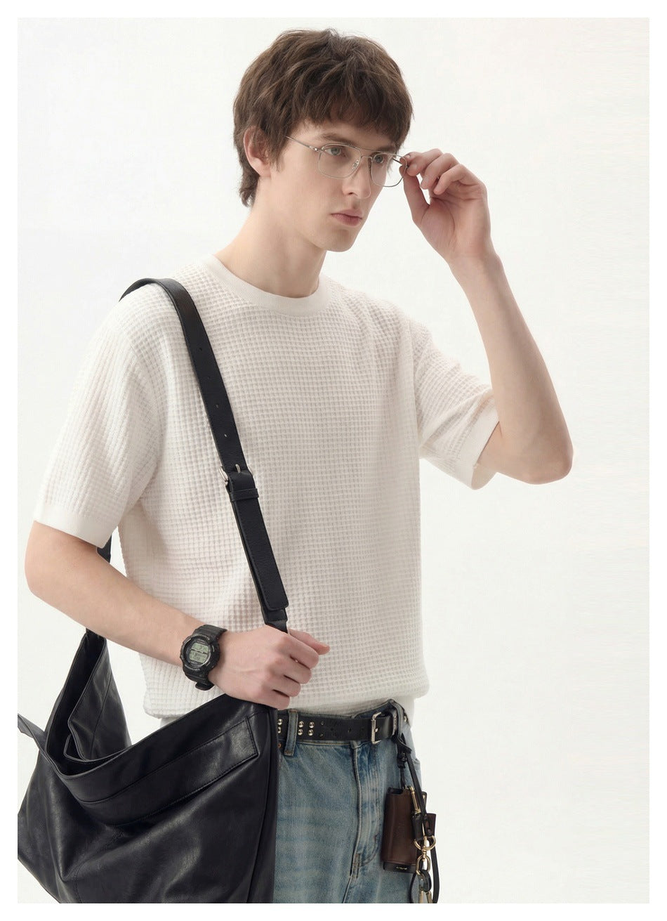 Model wearing a white textured short-sleeve shirt and carrying a large black shoulder bag.