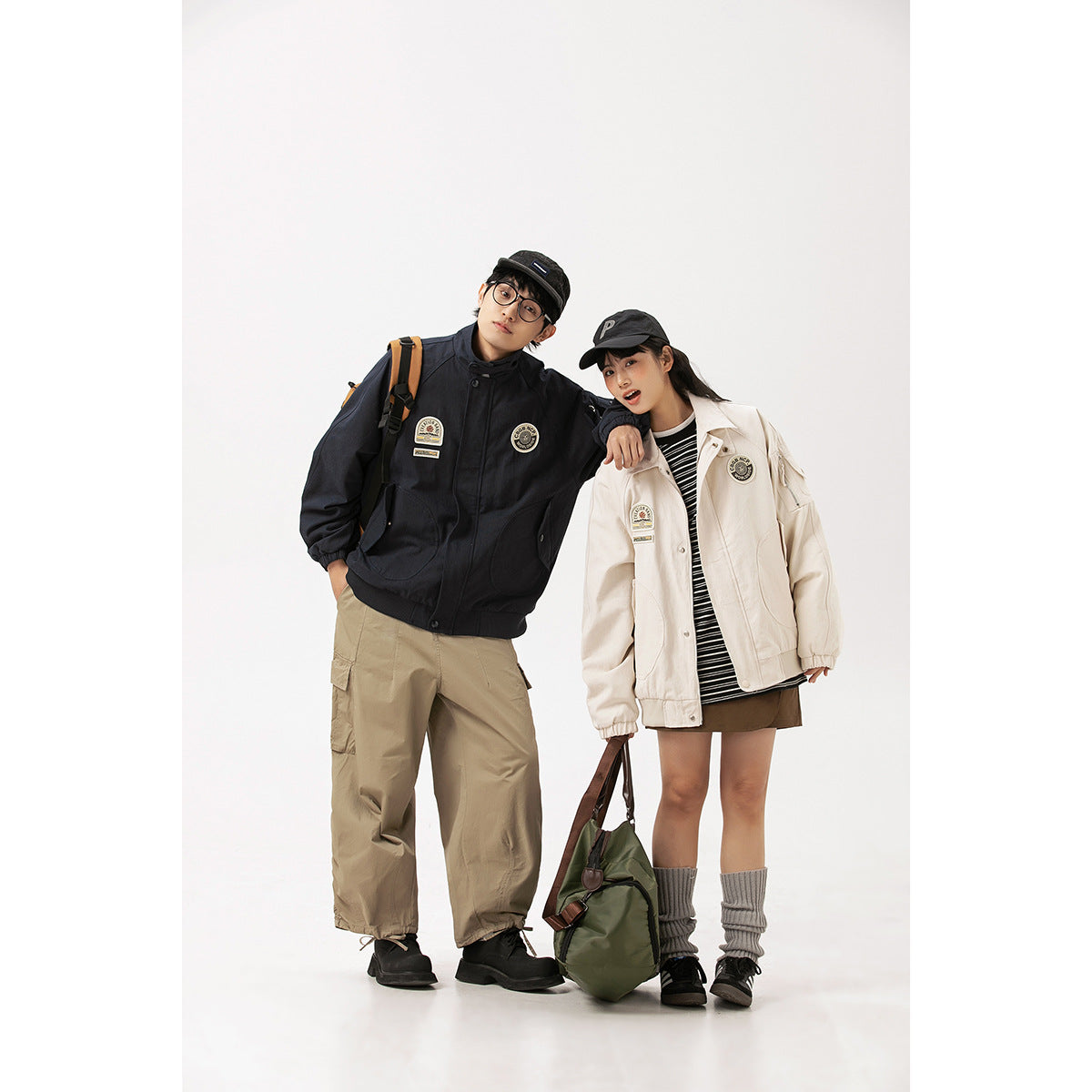 Two models wear oversized dark navy and cream patch jackets with casual outfits against a plain studio backdrop.