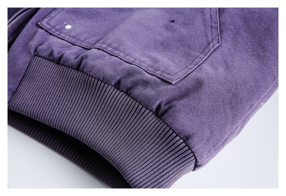 Close-up of a purple jacket's ribbed hem and stitched pocket, with small paint-like marks.