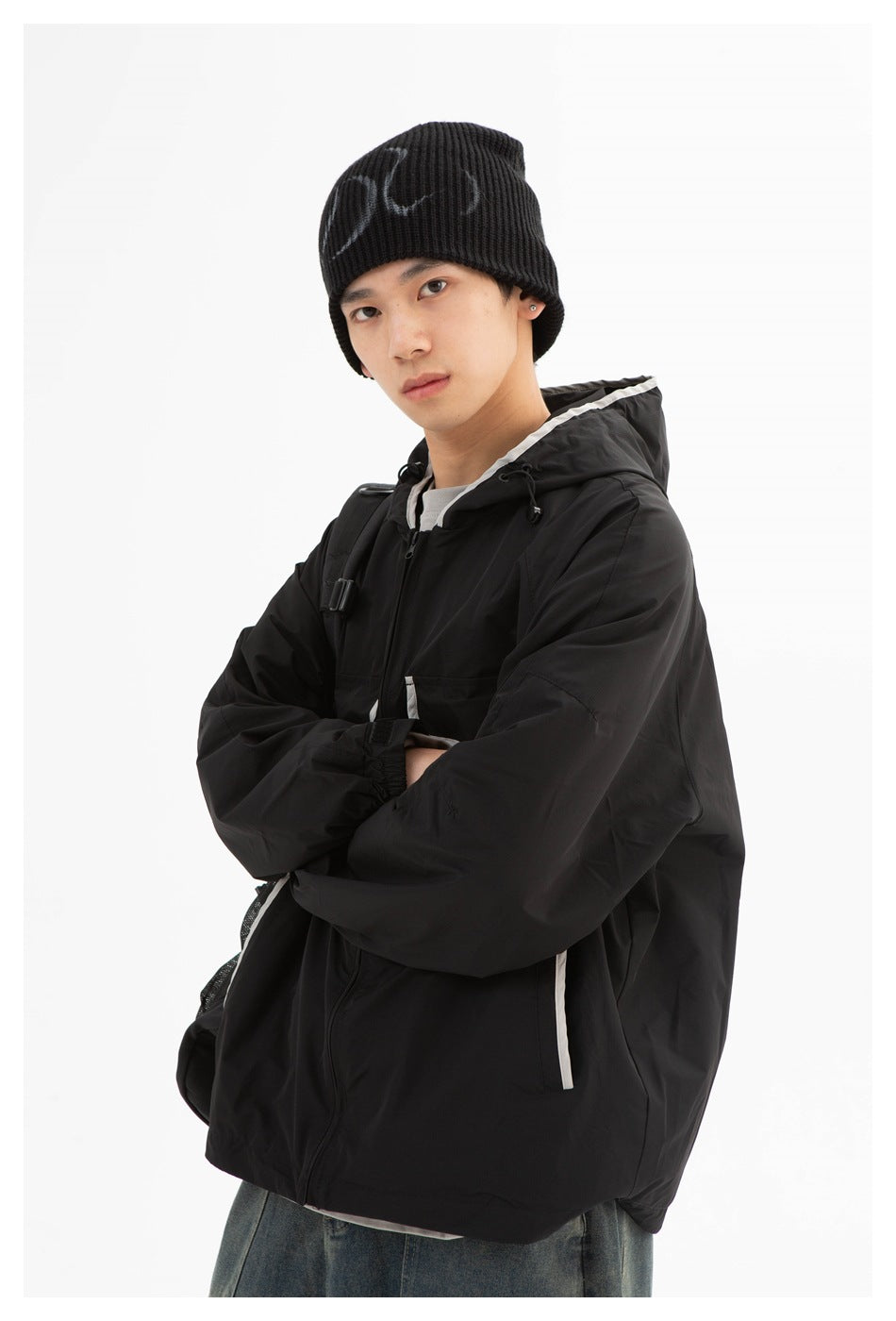 Closer view of a man wearing a black hooded jacket with white trim and a black beanie.