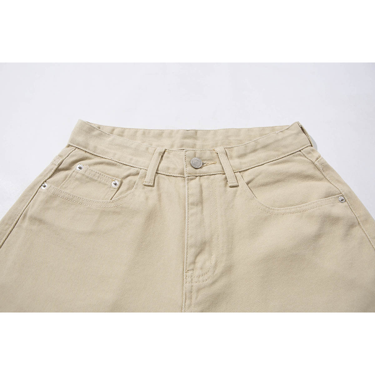 Close-up of beige pants front waistband with button, belt loops, fly, and front pockets.