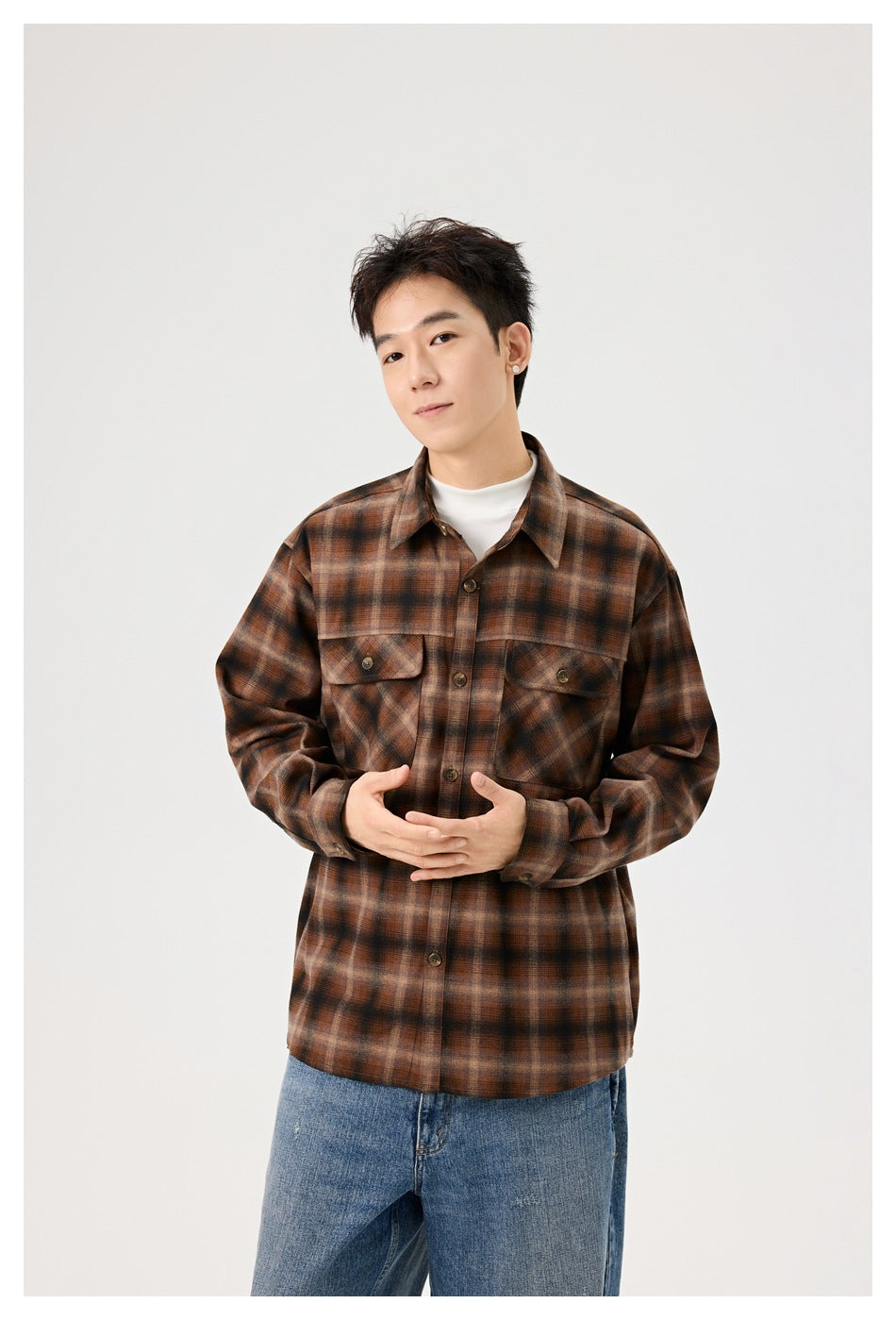 Waist-up view of a model wearing a brown plaid button-up overshirt with two flap chest pockets over a white top.