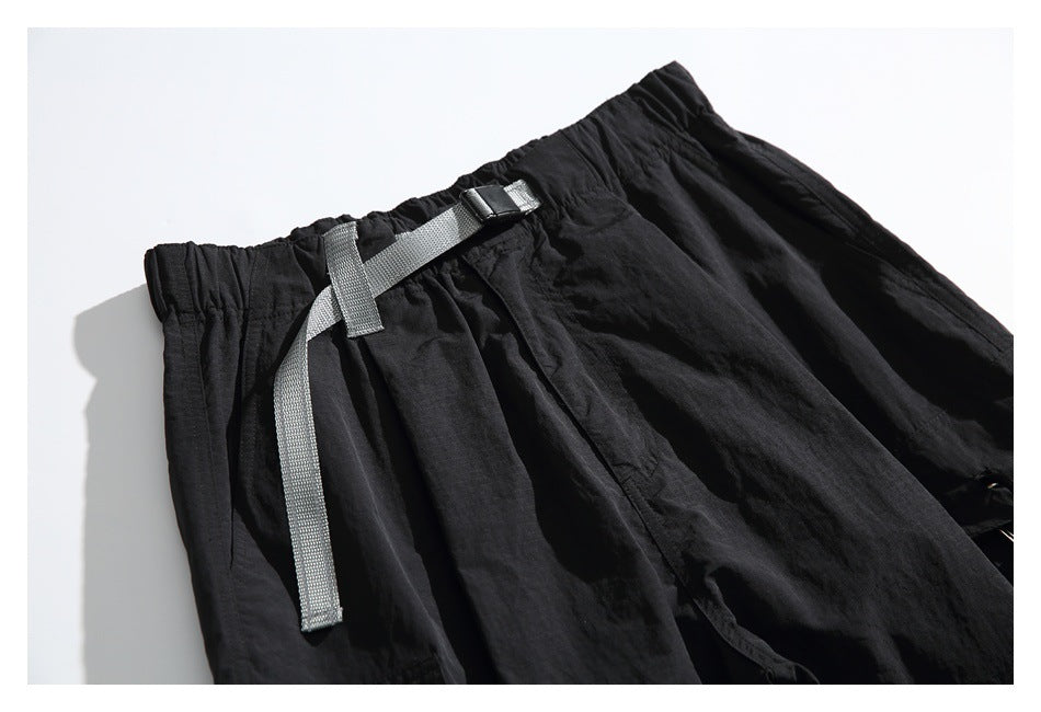 Close-up of black pants with an elastic waistband and a gray adjustable webbing belt.