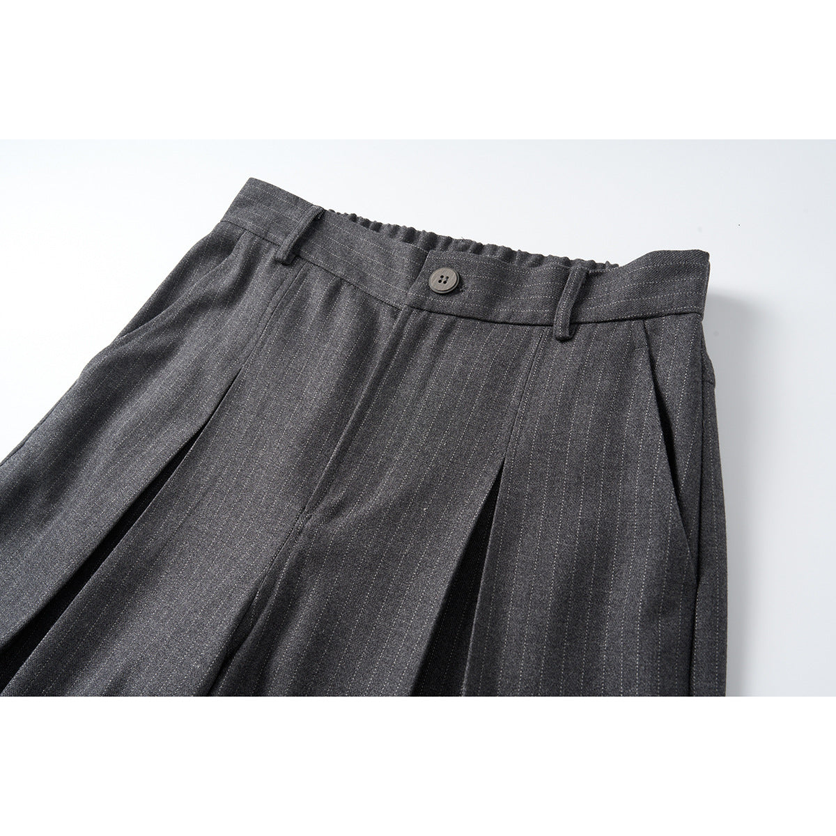 Close-up of dark charcoal pinstripe trousers showing the buttoned waistband, belt loops and front pleats.