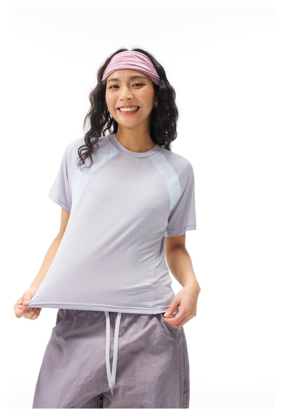 Model wearing a pale lilac short-sleeve athletic top with light contrast panels and matching headband.
