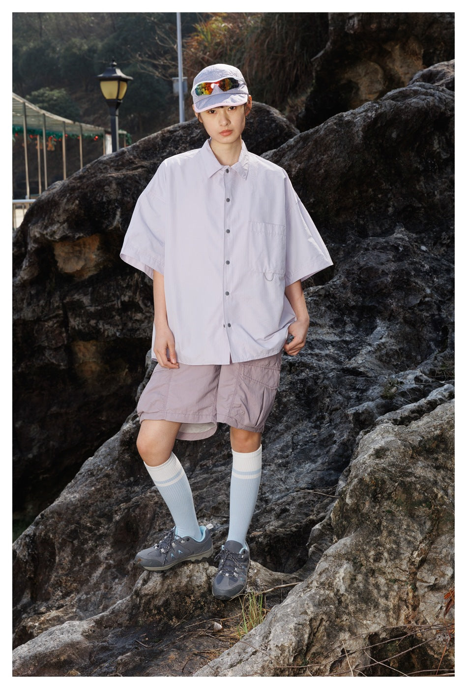 A woman faces the camera in a pale lavender short-sleeve button-up shirt and matching cargo shorts.