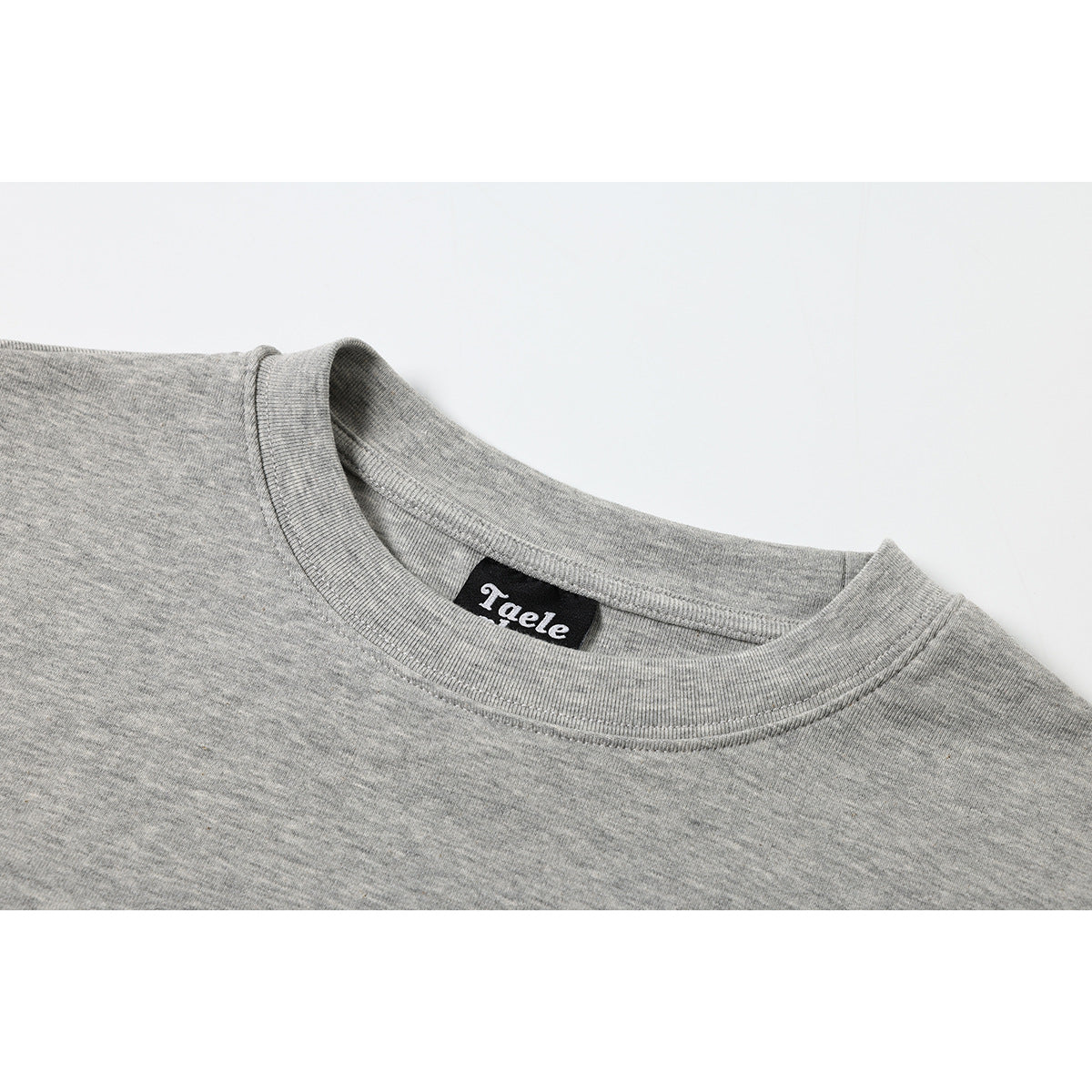 Close-up of a heather gray T-shirt’s ribbed crew neckline and sewn black Taele label.