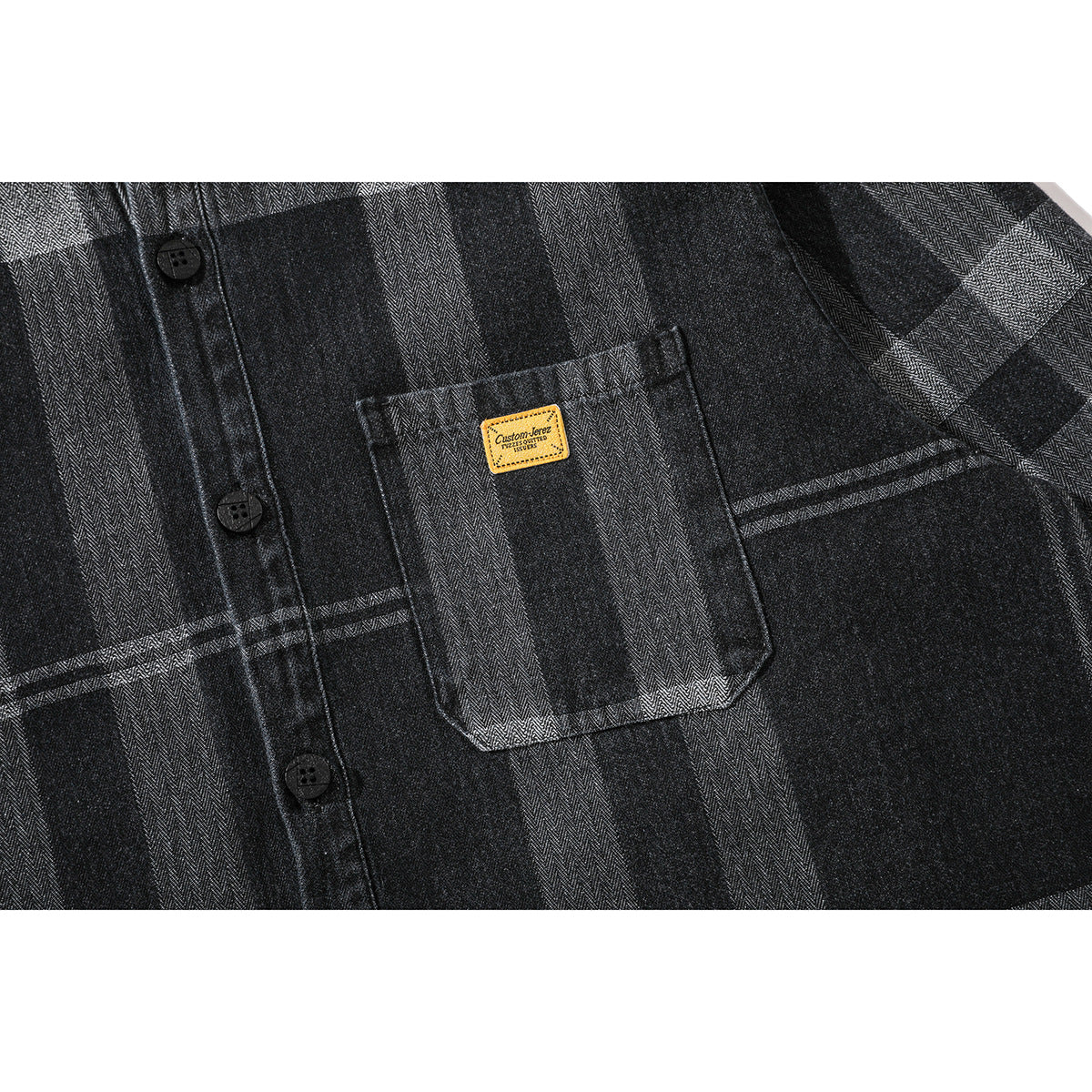 Close-up of a black-and-gray plaid shirt’s chest pocket, yellow patch, buttons, and fabric pattern.