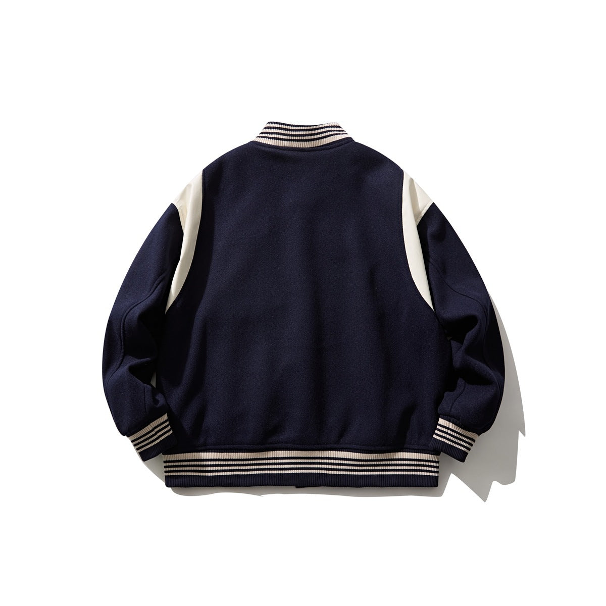 Back view of a navy varsity jacket with cream shoulder panels and cream-striped ribbed collar, cuffs, and hem.