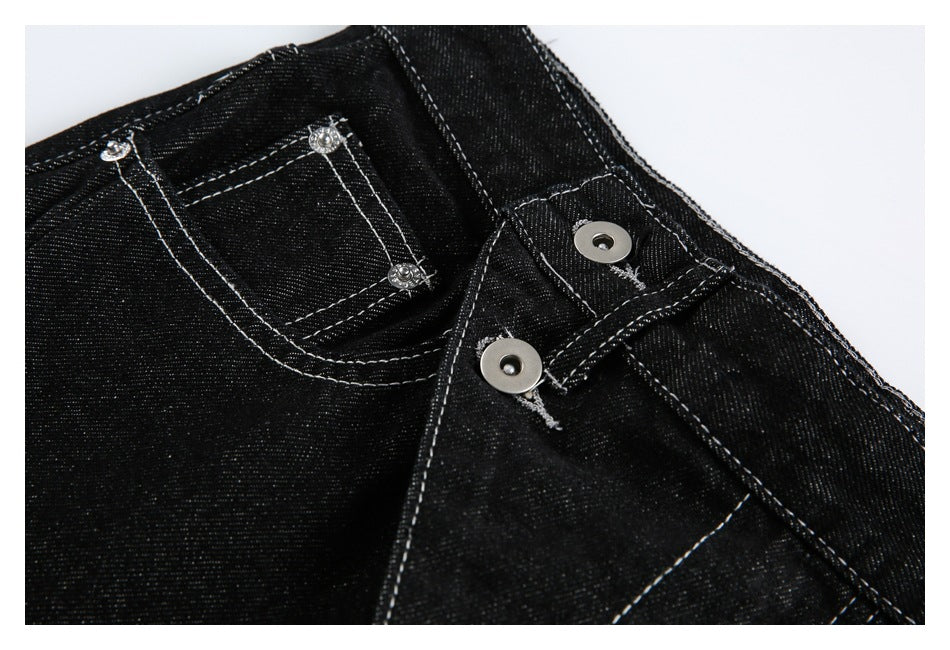 Close-up of black jeans showing the waistband, small pocket, metal buttons, and contrast stitching.