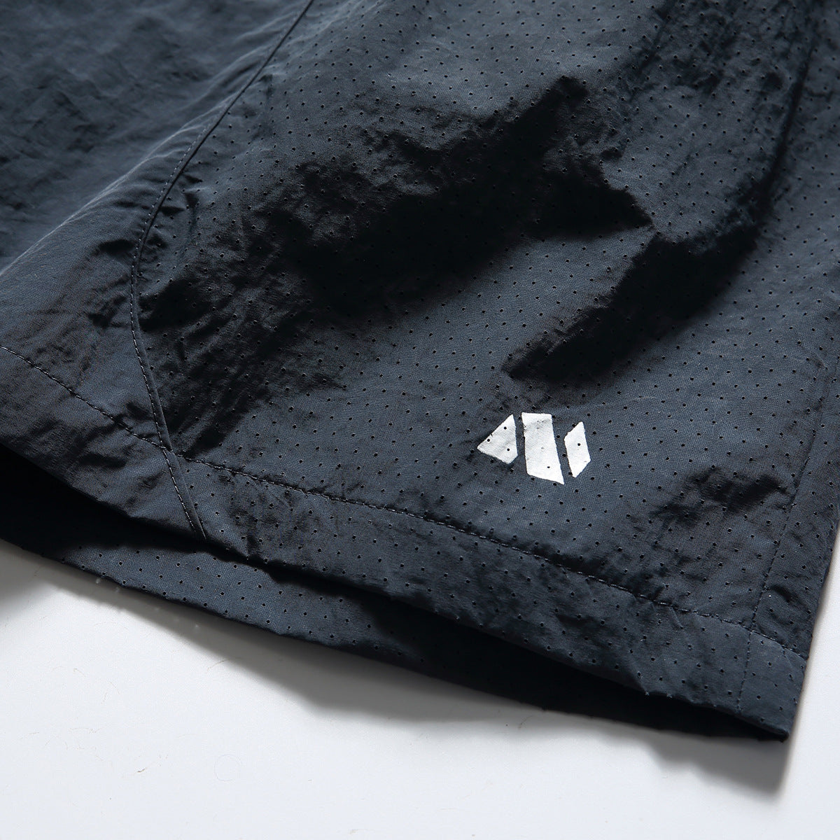 Close-up of dark navy shorts showing perforations, curved stitching, and a small white geometric logo.