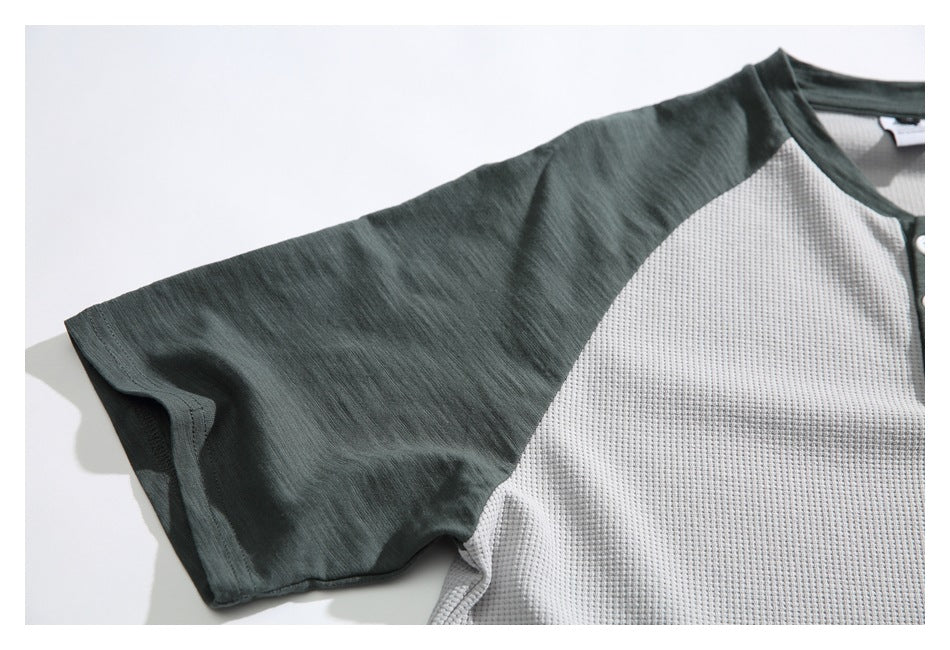 Close-up of a dark green raglan sleeve joined to the light gray textured body of a shirt.