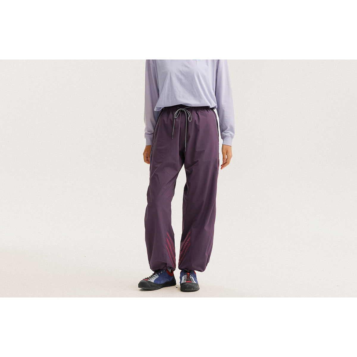 Cropped model wearing plum-purple drawstring pants with red accents near the ankles, shown from the front.