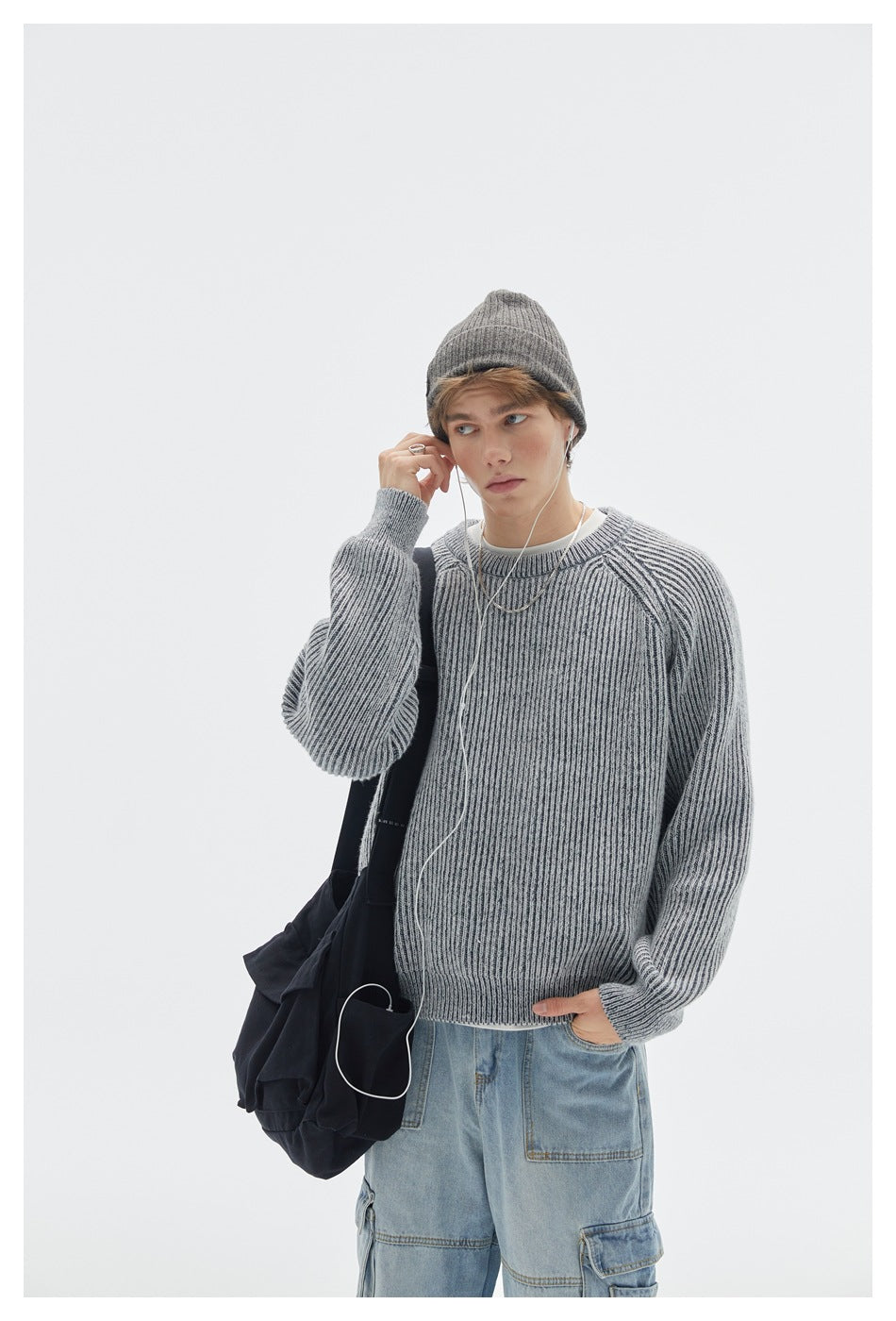 Upper-body view of a model wearing a light gray ribbed raglan sweater and beanie with a black shoulder bag.