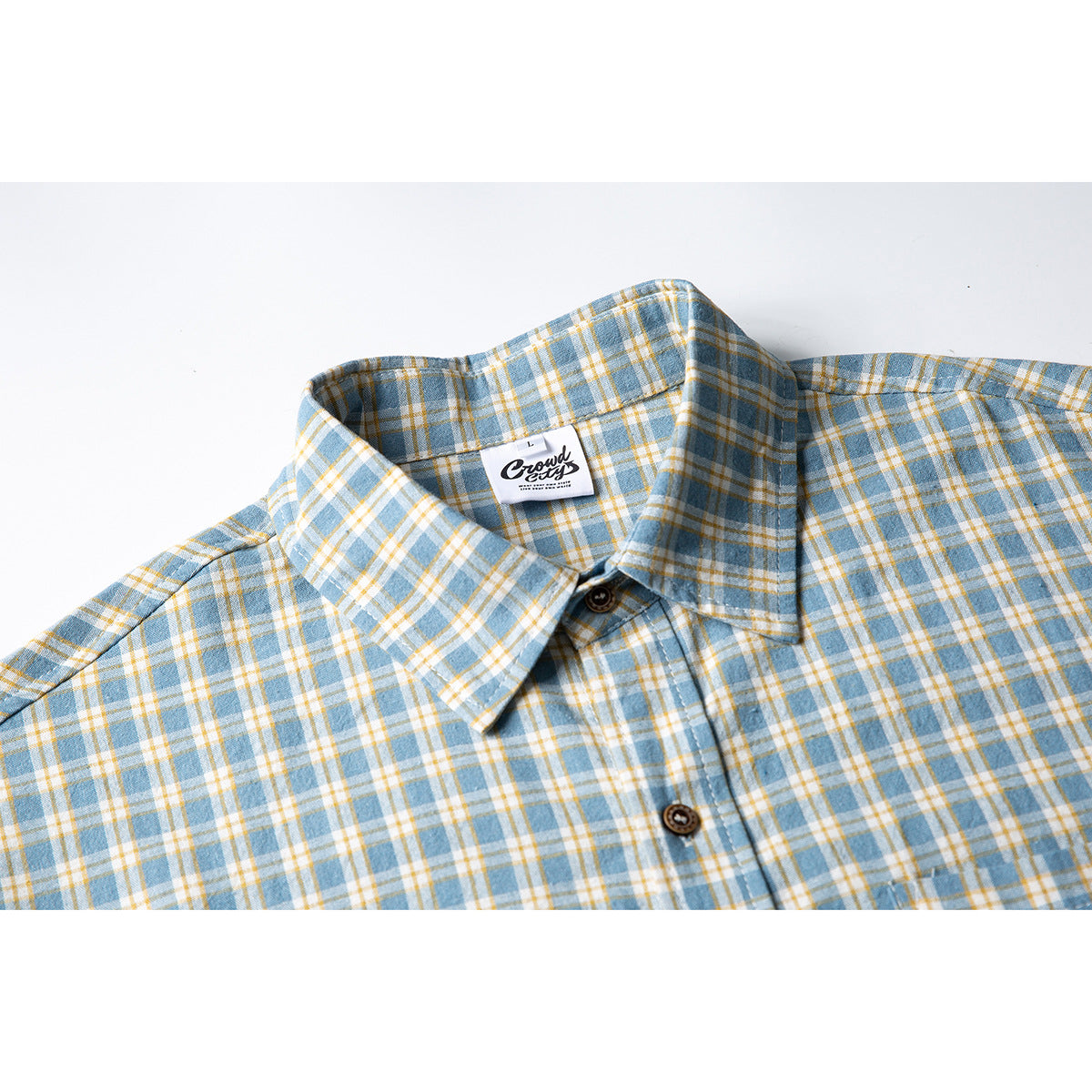 Close-up of a blue, white, and mustard plaid short-sleeve shirt collar, buttons, and inner neck label.