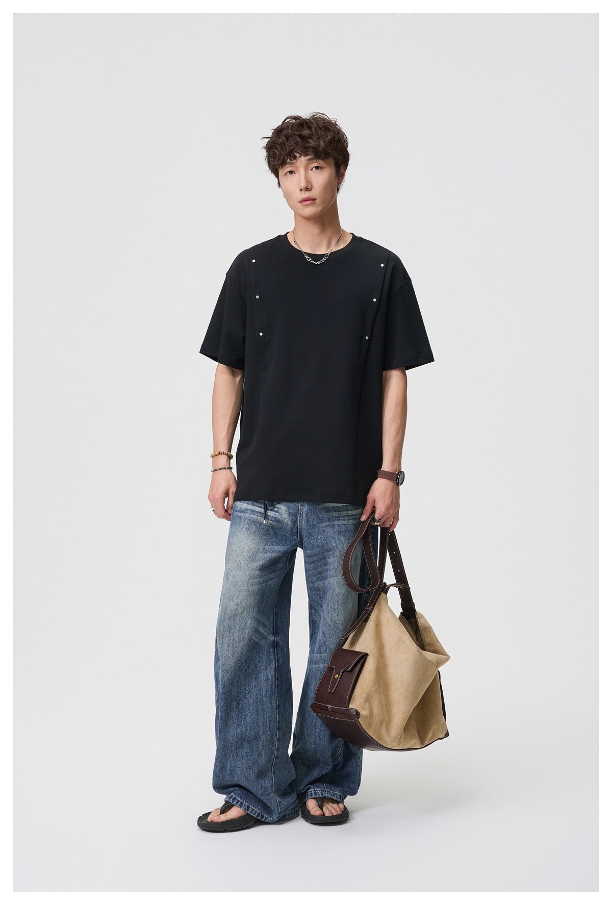 Full-length front view of a model wearing a black T-shirt with silver studs and wide-leg jeans.