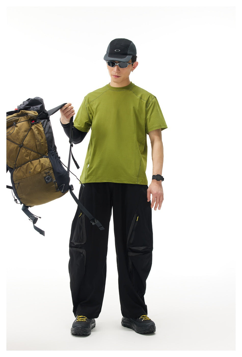 Model wearing an olive green short-sleeve shirt and black cargo pants, with a hiking backpack.