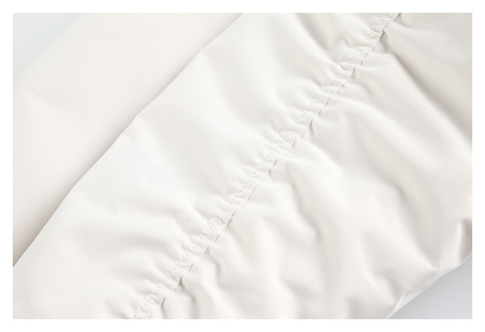Close-up of an ivory jacket seam with gathered stitching and softly folded fabric.
