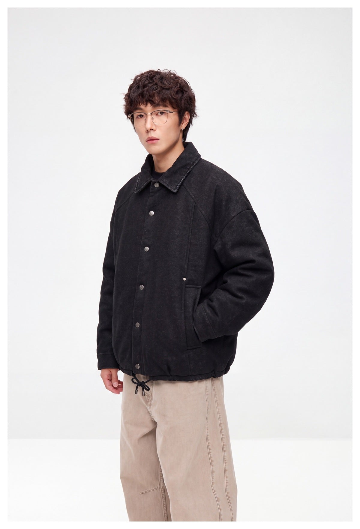 Model wearing a black button-front jacket with a pointed collar and drawstring hem, shown at an angle.