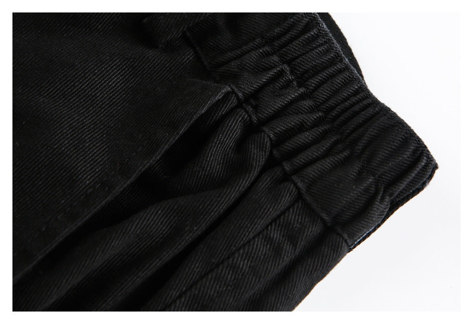 Close-up of the gathered, elasticized side waistband on black trousers.