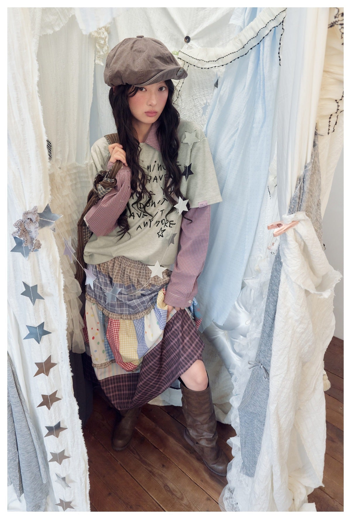 Model in apricot polo-collar layered-look top with pink check sleeves, a patchwork skirt, brown boots and star garlands