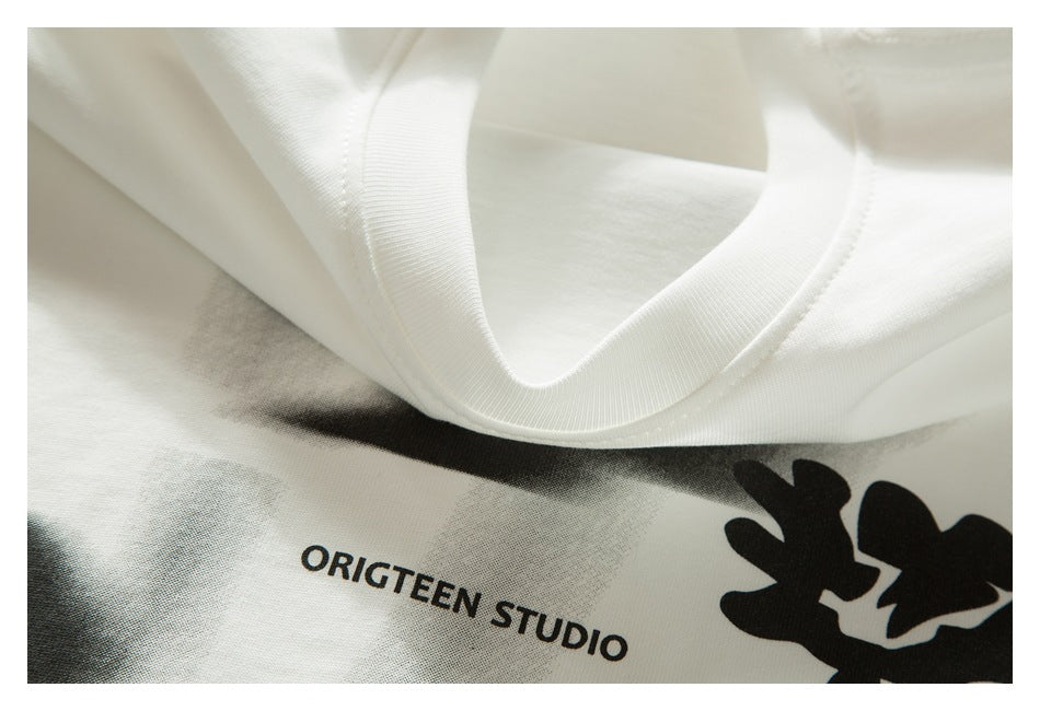 Close-up of a white shirt's ribbed collar and part of its black flower graphic and “ORIGTEEN STUDIO” print.