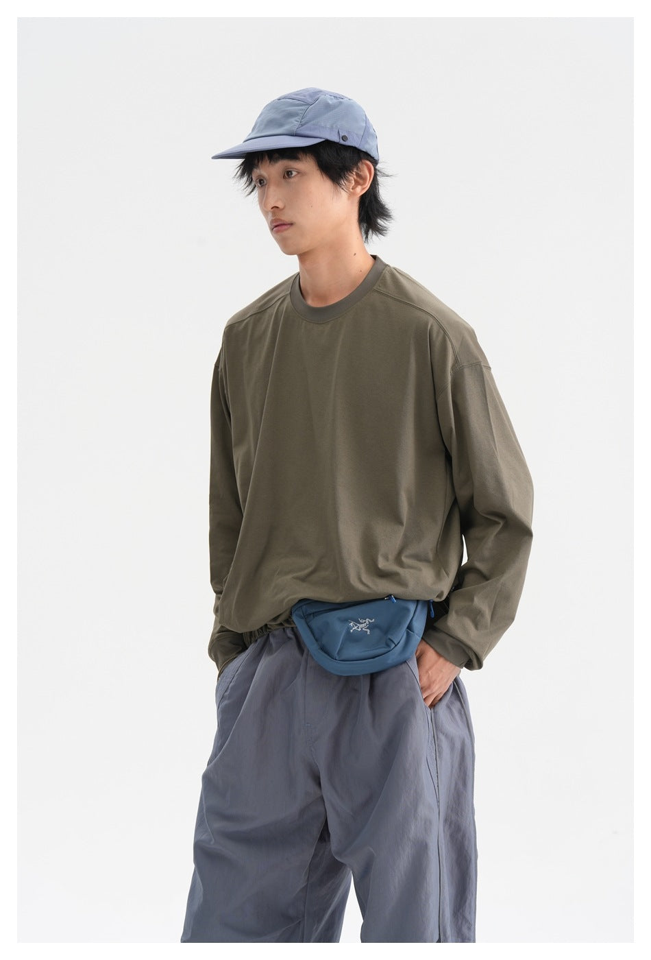 Closer view of a man wearing an olive long-sleeve shirt, slate-blue trousers, blue cap, and blue waist bag.