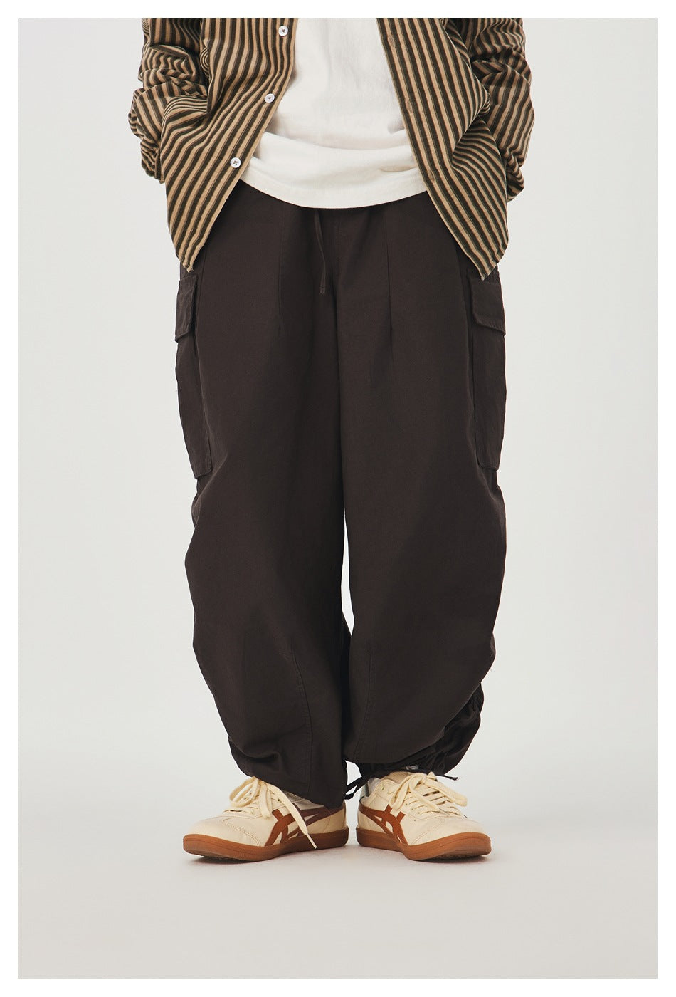 Front view of a model wearing loose dark brown cargo pants with side pockets and gathered hems.
