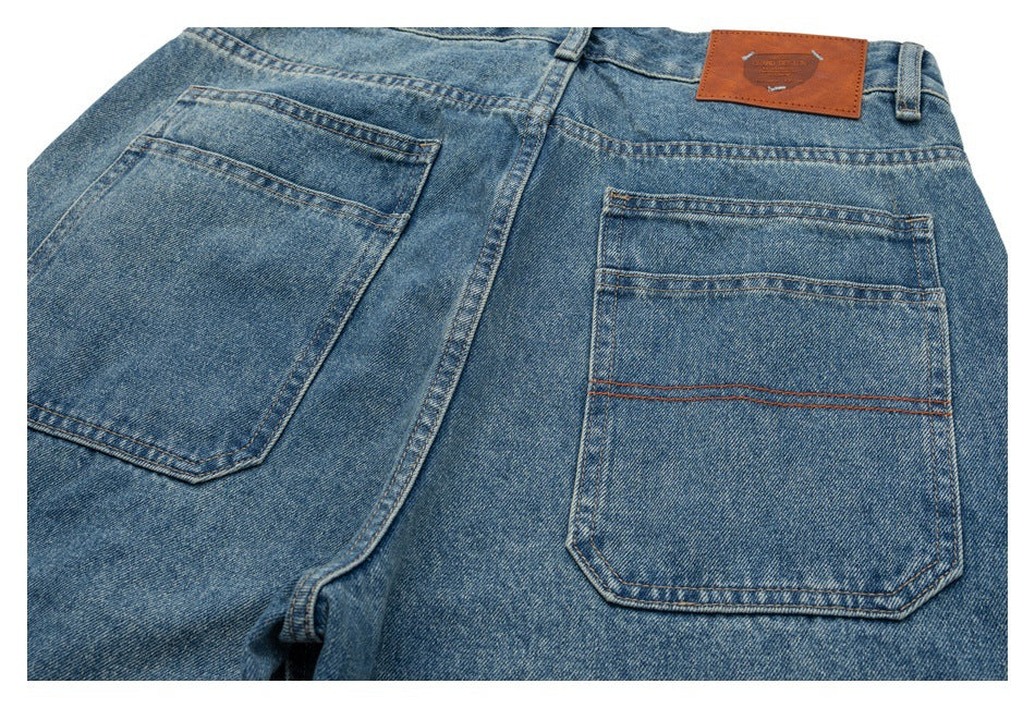 Close view of the back of blue jeans, showing two patch pockets, contrast stitching, belt loops and a brown waistband patch.