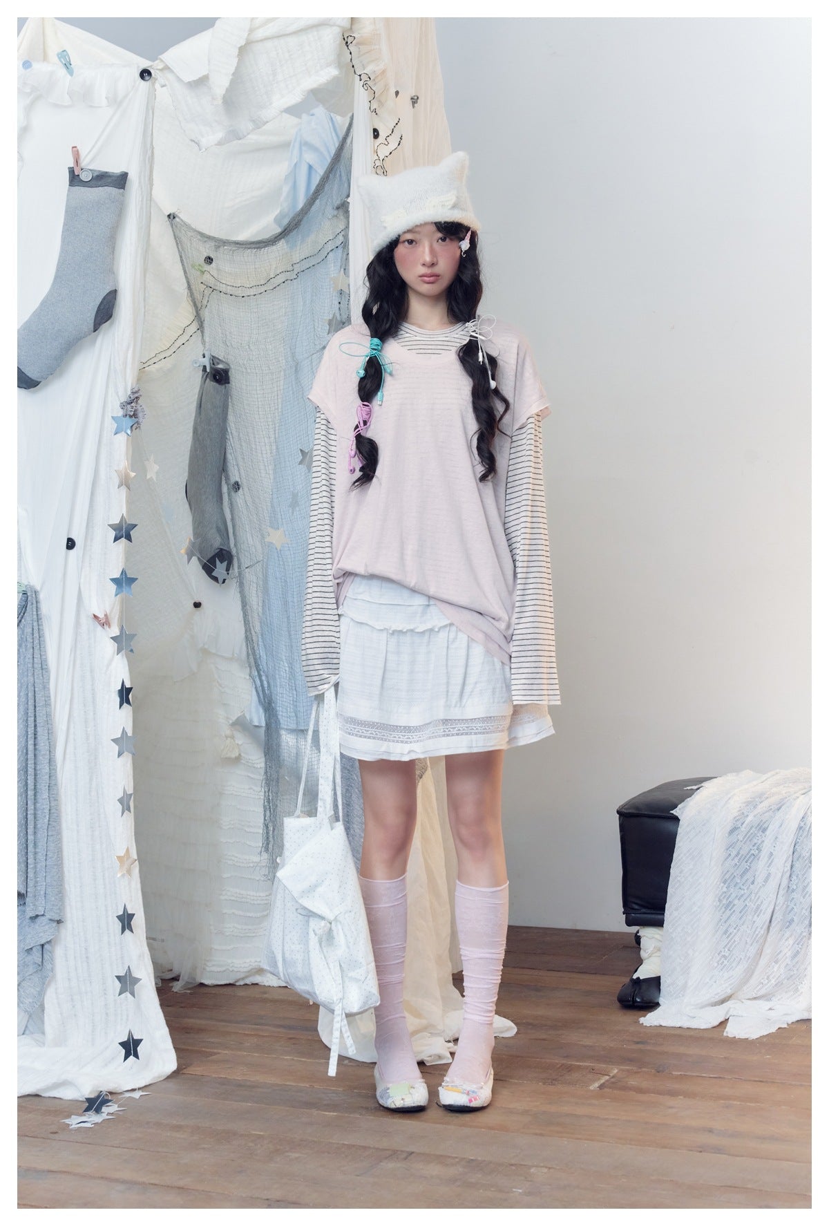 Model wearing pink layered striped top with white ruffled skirt, pink socks and white knit cat-ear hat, front view