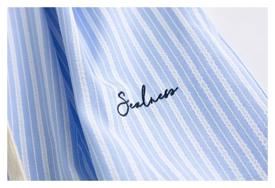 Close-up of dark cursive embroidery on light blue and white striped shorts.