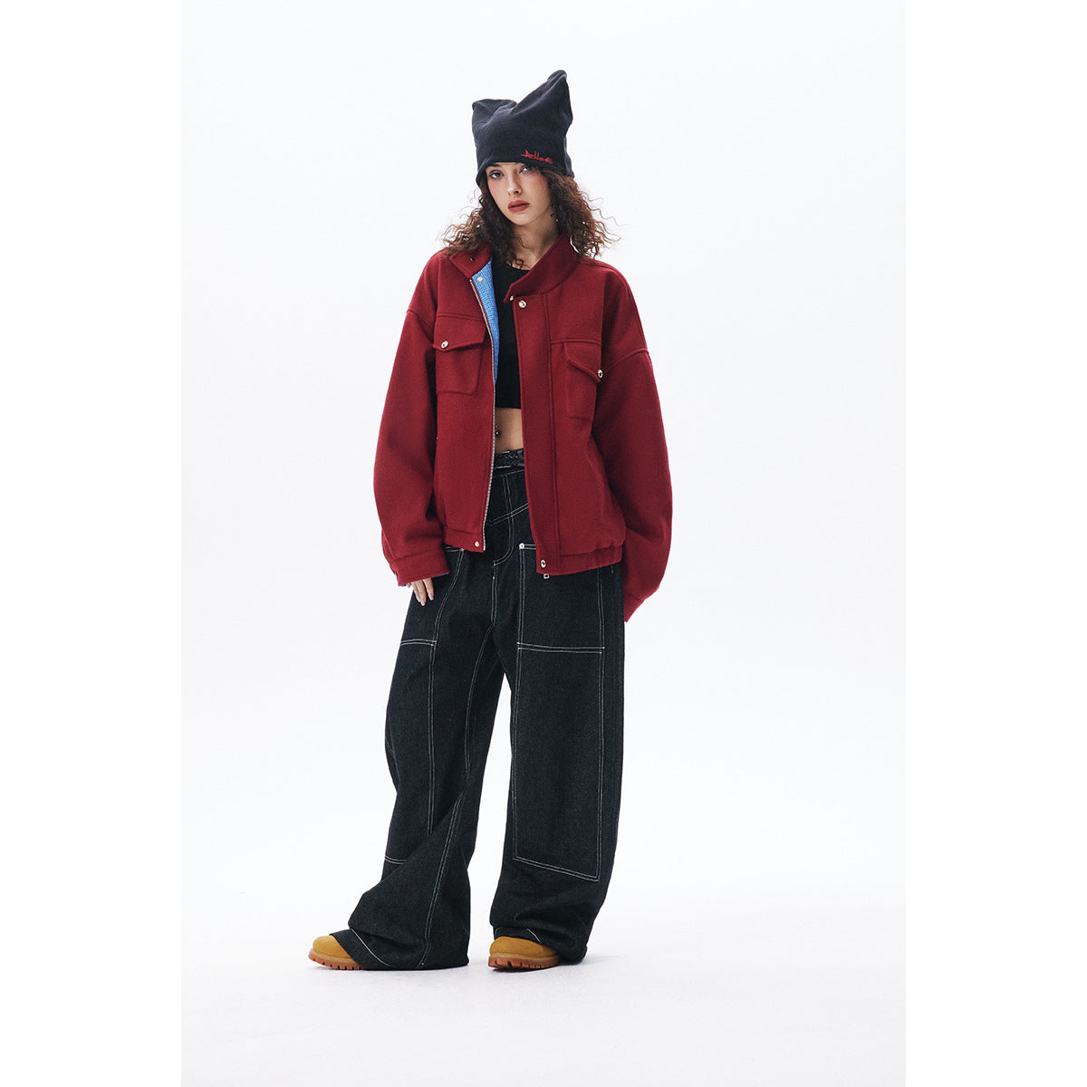 Model wearing a burgundy snap-front jacket with flap pockets, black wide-leg jeans, and a black pointed beanie.