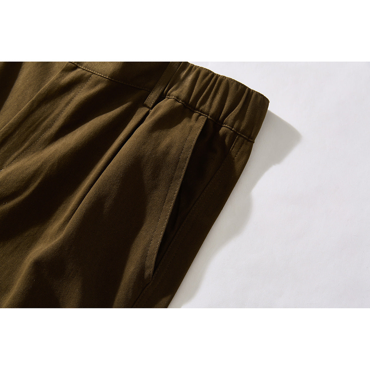 Close-up of dark brown trousers showing the elasticated waistband, belt loop and side pocket.