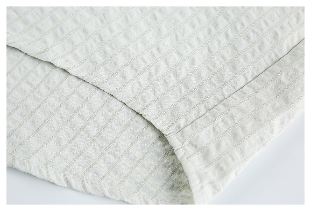 Close-up of the ivory garment's striped fabric and stitched, folded hem.