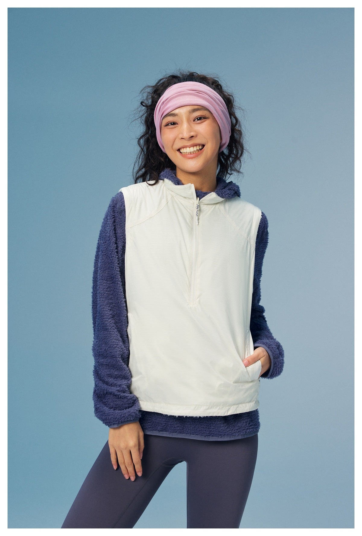 Front view of a model wearing an off-white zip vest over a navy fleece top and dark leggings.