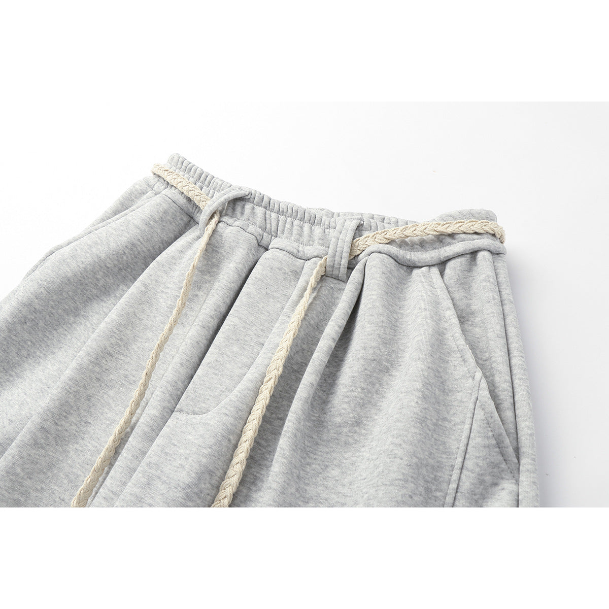 Close-up of light gray heathered sweatpants with an elastic waist, cream braided drawstrings, and front pockets.