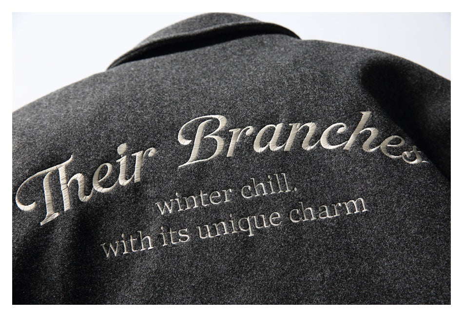Close-up of cream English embroidery on a charcoal gray coat, with a folded collar above.