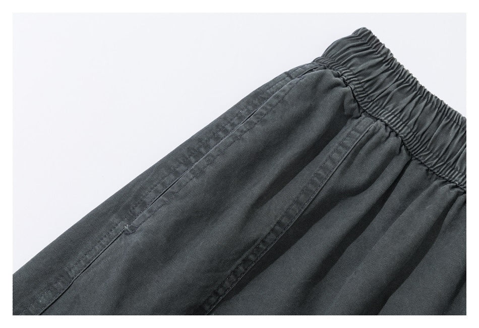 Close-up of the gathered elastic waistband and stitched seams on dark charcoal pants.
